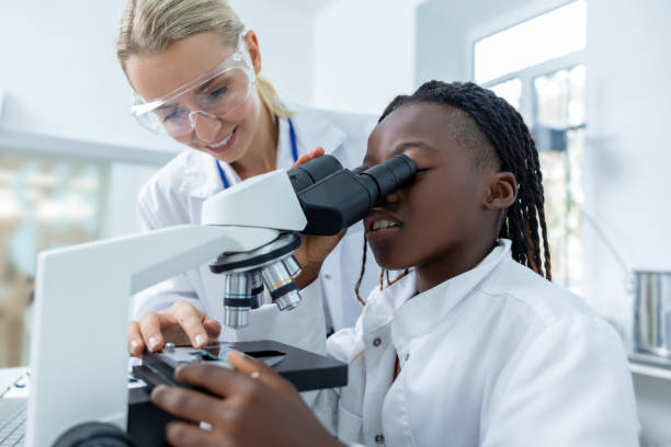 istock Blonde teacher helping a student in a protective glasses to scrutinize substance in a microscope 2193902152