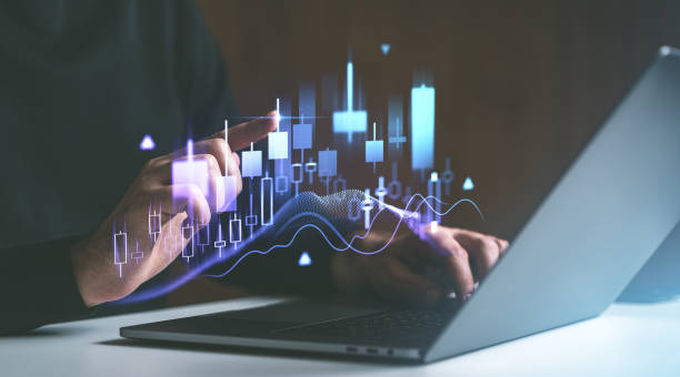 istock Businessman's hand interacting with a digital candlestick chart and financial graph on a laptop screen in a dark background. 2193904584