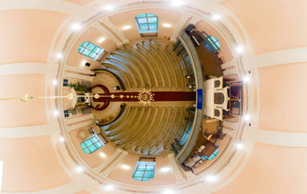 360 degree view of a church interior featuring arched windows, pastel ceiling, central chandelier, organ, red carpet, and symmetrical pew arrangement.