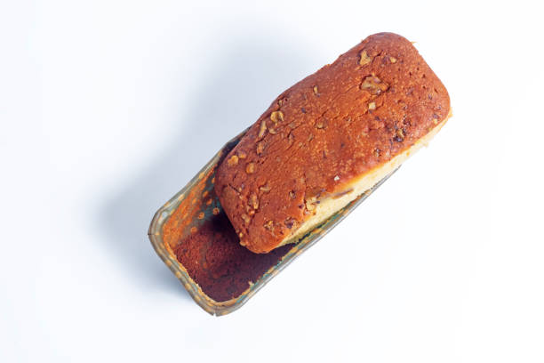 Top view of freshly baked banana bread with nut toppings on a white background, in a cardboard box