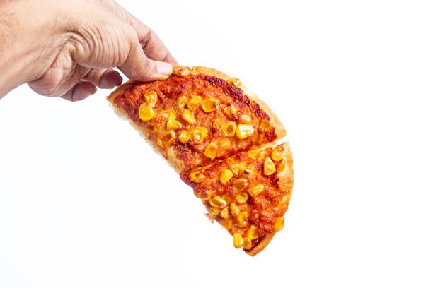 Hand holding a slice of corn topped pizza against white background, closeup