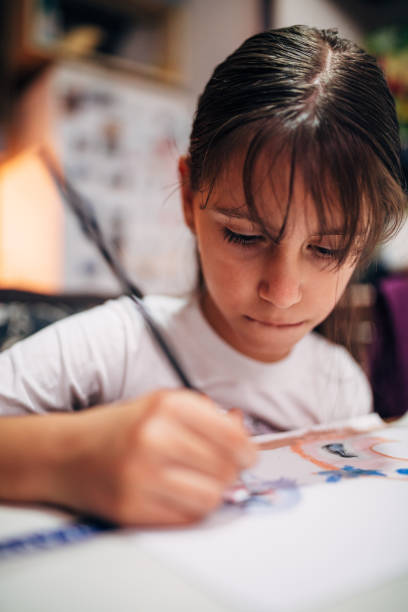 A child immersed in creative painting draws strokes with a brush on paper indoors