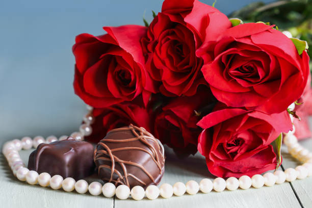 Beautiful red long stem roses with chocolate candy and real strand of pearl necklace.  Selective focus on center pieces of candies. Blurred foreground and background.