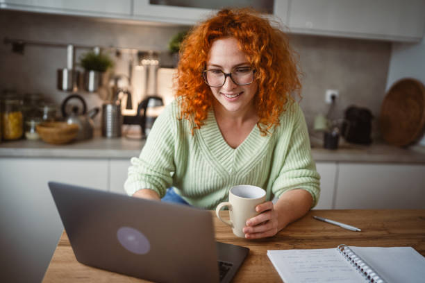 istock adult woman with coffee mug work on laptop computer at kitchen happy 2193926332