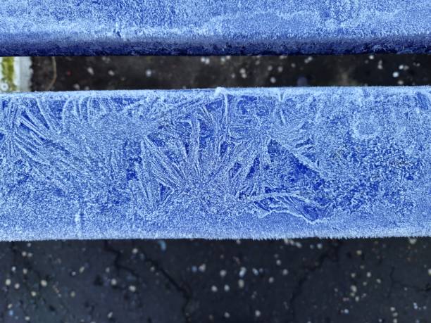 Frost pattern on a blue metal seat bench, Glasgow, Scotland. The metal seat at the railway station platform, and covered with a frost pattern. At the background black station platform surface can be seen.