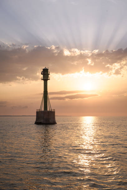 istock Lighthouse in the Ocean at Sunset with Sun Rays 2193931532