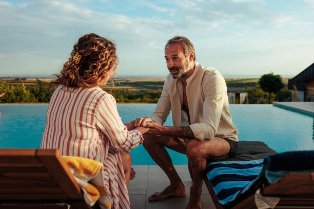 istock Mature couple holding hands and talking by infinity pool during sunset 2193940278