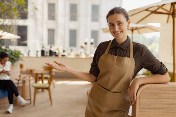 istock Smiling Cafe Worker Welcoming Customers in an Outdoor Coffee Shop Setting 2193940849