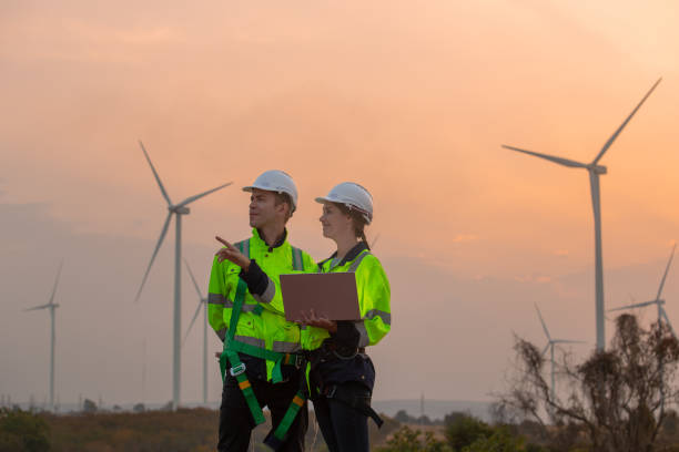 istock Team engineer wearing safety uniform holding laptop discussed plan about renewable energy at station energy power wind in evening when sunset. Technology environment reduce global warming problems. 2193943053