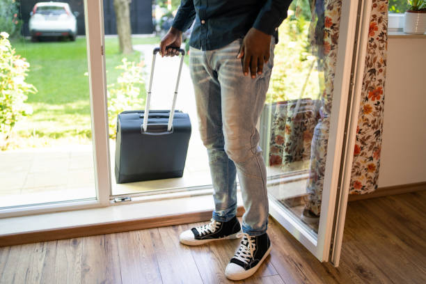 A man from the waist down entering the glass doors of his accommodation while dragging a suitcase behind him