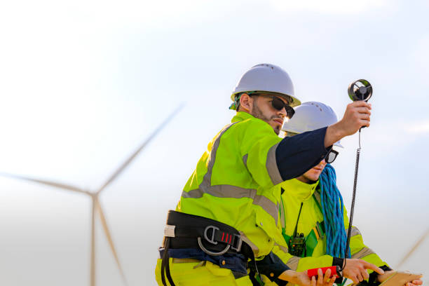 istock Two engineers wearing high visibility safety jackets and helmets measure wind speed with an anemometer and analyze data on a tablet at a renewable energy site. The cloudy sky adds depth to the scene. 2193946250
