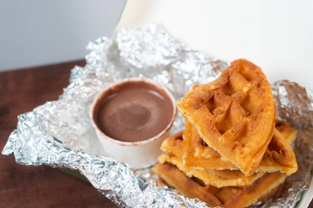 A delicious serving of waffles stacked on a piece of foil, accompanied by a small cup of chocolate sauce for dipping.