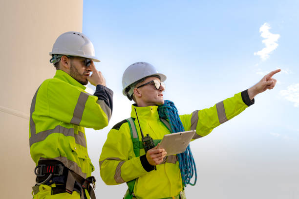 istock Two engineers in high visibility gear and hard hats observe a wind turbine and communicate via radio at a wind energy site. The image highlights teamwork, safety, and renewable energy production. 2193948879