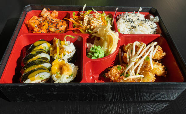 istock Japanese Lunch in Bento Box with Deep-Fried Squid Rings, Sushi Rolls, Salad, Rice, Pickled Ginger 2193949576