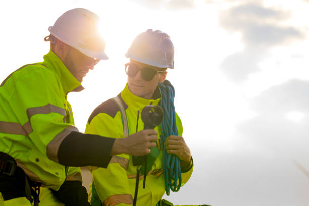 istock Two engineers wearing high visibility safety jackets and helmets measure wind speed with an anemometer and analyze data on a tablet at a renewable energy site. The cloudy sky adds depth to the scene. 2193950274