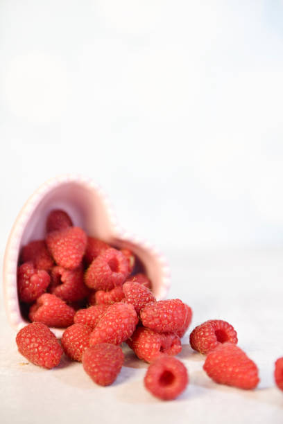 istock Fresh raspberries spilling from a pink heart-shaped bowl on a wh 2193959473