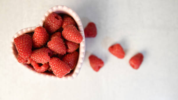 istock Fresh raspberries in a pink heart-shaped bowl on a light surfac 2193959476