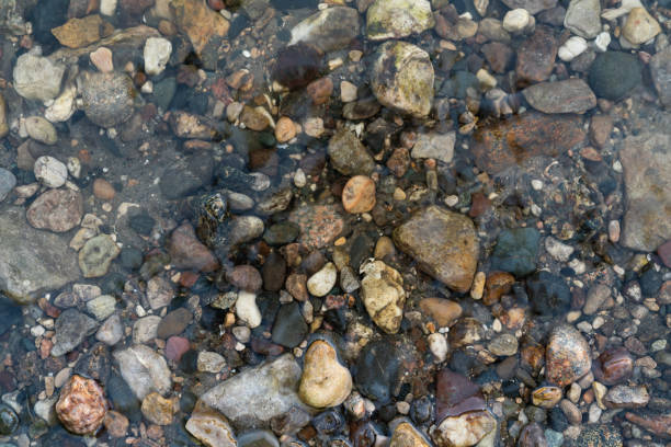 A close-up view of clear water gently rippling over colorful pebbles at the bottom of a lake, highlighting the natural textures and transparency of the water.