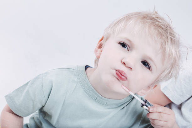 Toddler enjoying a playful moment while older sibling applying lip gloss, discovering the world of makeup and beauty. Innocent exploration and bonding between sisters captured in a joyful setting