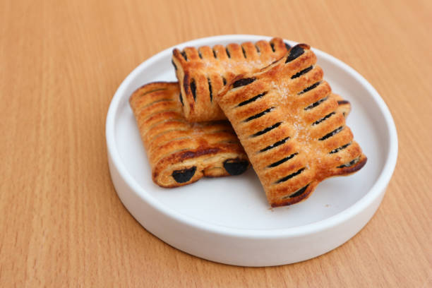 Three golden brown pastries with a chocolate filling sit on a white plate on a wooden table.