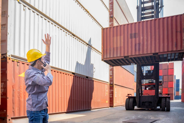 istock foreman control loading containers box from cargo freight ship,holding walkie talkie and hand up for direction the forklift handling container stacker craine 2193975186