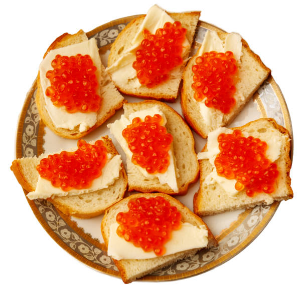 A plate of bread with red caviar on top. The caviar is spread out on the bread, and there are several pieces on each slice. The plate is white and has a gold rim, giving it an elegant appearance