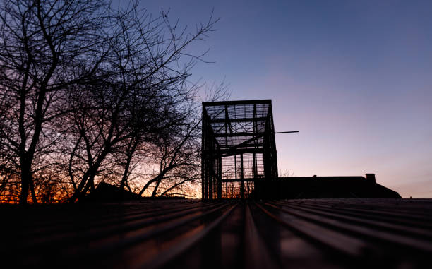 A large building with a tall tower is silhouetted against a dark sky. The sky is filled with clouds and the sun is setting