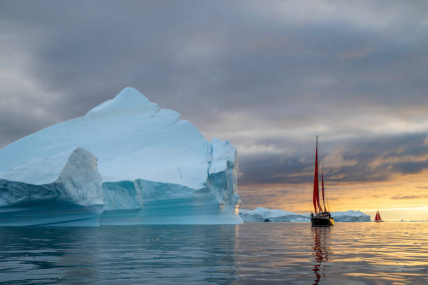 istock red sailboat sailing among floating icebergs in Disko Bay glacier with orange sunset during polar summer midnight solar season. Ilulissat, Greenland 2193977576