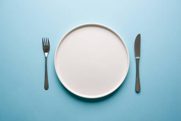 istock Top view of empty ceramic white plate and cutlery on blue background 2193978978