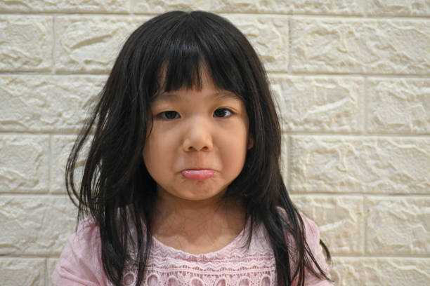 Portrait of sad cute Asian little girl sitting alone on floor near sofa at home