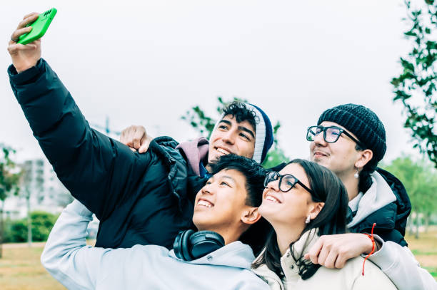 istock Four cheerful multi-ethnic students are taking a selfie together outdoors, embracing friendship and diversity, smiling and looking up at the smartphone 2193981757