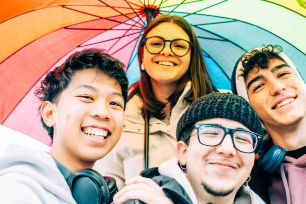 istock Diverse college friends gathering closely, sharing bright rainbow umbrella, expressing camaraderie and multicultural connection with genuine smiling expressions 2193981797