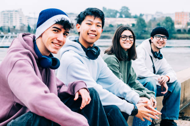 istock Diverse high school students relaxing together, wearing headphones, sitting side by side on urban wall, sharing friendly moment and smiling warmly 2193981805