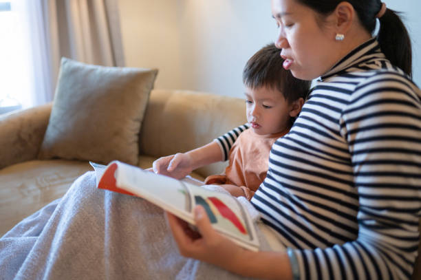 istock Mother and child read on modern brown sofa by lamp light. 2193987331
