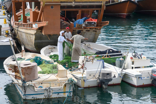 Khasab, Oman - January 1, 2025: Omani fishermen diligently preparing their fishing nets by the harbor, capturing the essence of traditional maritime life.