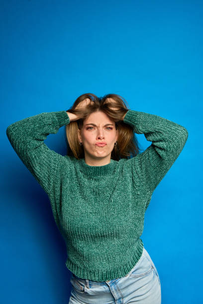 istock Young woman pulling her hair out in frustration on blue background 2193989410