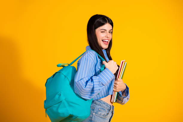 istock Trendy young female student posing with books and backpack on yellow background, showcasing a stylish casual look 2193989932