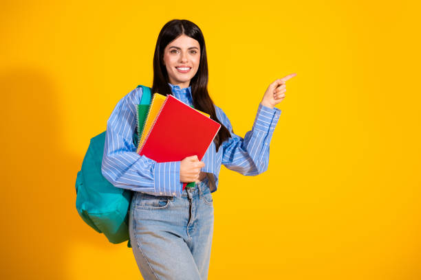 istock Young female student posing with books on a vibrant yellow background, dressed casually and smiling confidently 2193989970