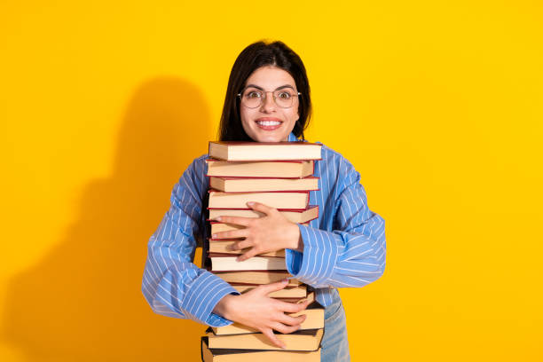 istock Young woman holding a stack of books with a joyful expression against a yellow background 2193990054