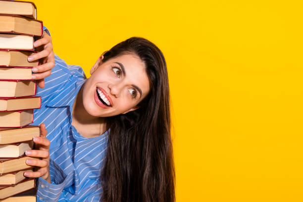 istock Smiling young woman holding a stack of books while standing against a vibrant yellow background 2193990057