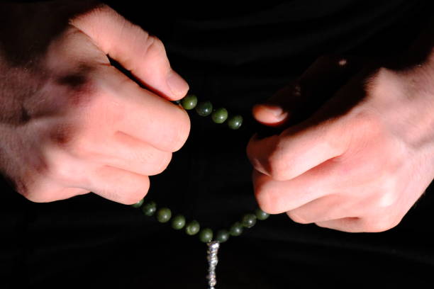 Close-up hands holding rosary beads on a black background. Ramadan, Islamic holy days, Miraj Kandili, Eid al-Fitr, Eid al-Adha. To pray, to worship. Blessed days.