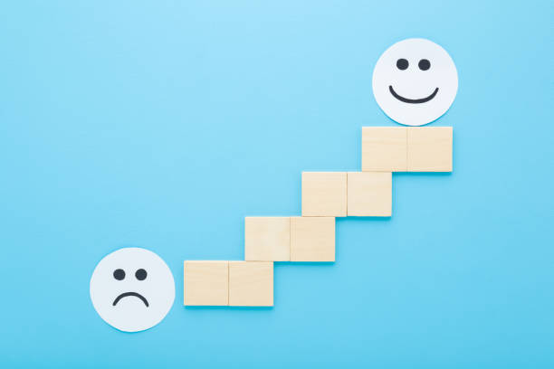 istock Sad and happy smiling faces and wooden bricks ladder on blue table background. Pastel color. Negative and positive expressions on white circle paper. People mood level concept. Closeup. Top down view. 2193993023