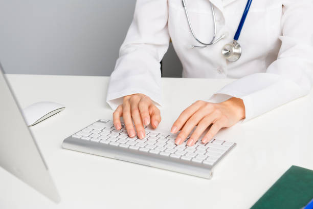 A medical professional wearing a white uniform working on a computer keyboard in a clinical or hospital environment, symbolizing modern healthcare technology and patient care.