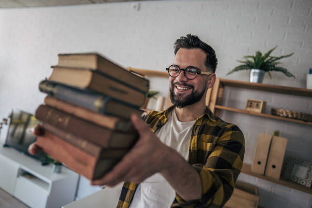 istock A man with glasses standing proudly as he effortlessly carries a large stack of books 2193995084