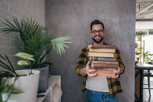 istock A man with glasses standing proudly as he effortlessly carries a large stack of books 2193995507