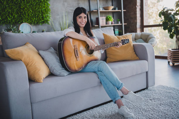 istock Young woman playing guitar while relaxing on a couch in a cozy living room 2193995521