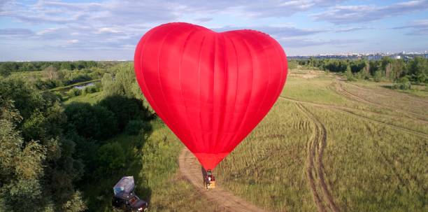 istock Red hot air balloon with a heart on it is flying over a field 2193996957