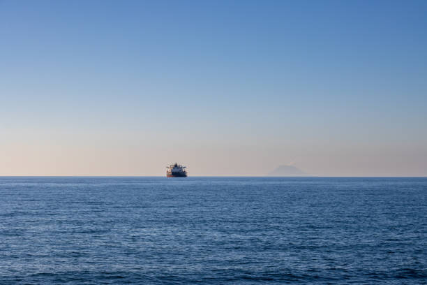 Calm dark blue water ot the Tyrrhenian (Mediterranean) sea. Big ship and Aeolian islands on the horizon. Blue sky with orange light in the early sunset. Caldera, Sicily, Italy.