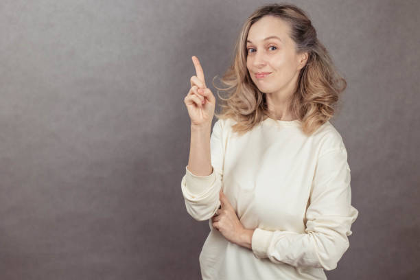 Young funny woman on gray background pointing finger up, copy space.