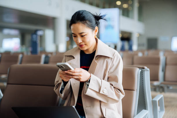 istock Asian young woman wearing trench coat and with suitcase using smartphone while waiting for her flight at airport terminal. Asian businesswoman on business travel. Lifestyle and technology. Business traveller. 2194003220